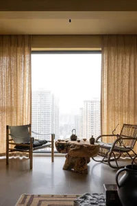 A minimalist living room with natural wood furniture and a large window overlooking a cityscape.