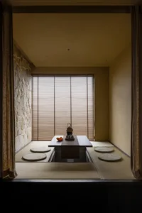 A minimalist tea room with bamboo flooring, wood walls, stone accents, and traditional seating.