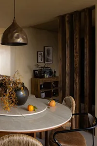 A modern dining room featuring a round marble table with a metal pendant lamp and wooden details.