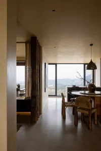 A modern dining room with wooden furniture and large windows showcasing a scenic view.