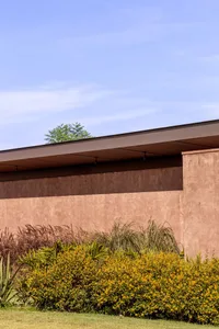 A modern residential exterior with a clay-colored wall and greenery.