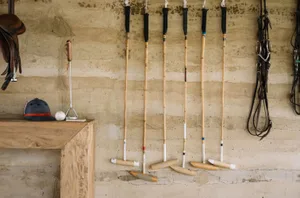 A workshop wall with a wooden table displaying polo mallets and other riding equipment.