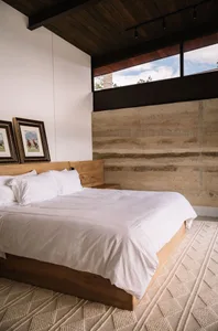 A modern bedroom featuring a wooden bed with white linens and a concrete wall.