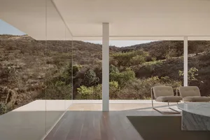 Interior of a modern residential space featuring large glass windows with a scenic view of hills and vegetation.
