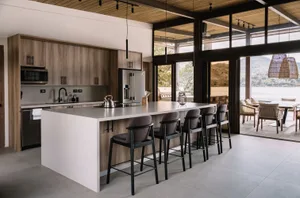 Modern residential kitchen with wooden cabinets, white countertops, and a large island with stools.