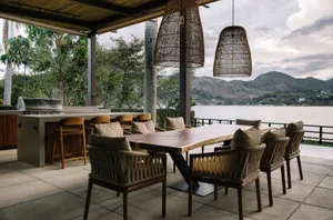 Outdoor dining area with wooden furniture and cushioned seating, overlooking a lake and mountains.