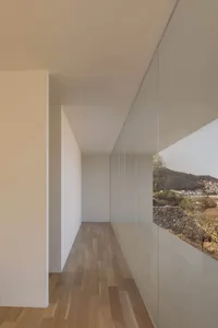 Interior of a minimalist residential space featuring glass walls, concrete floor, and wooden flooring.