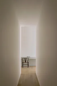 A minimalist workspace with a black chair and wooden desk in a corridor with illuminated walls.
