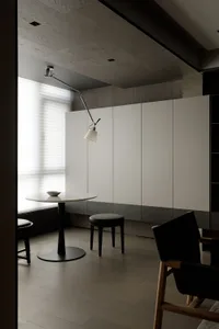 A modern kitchen featuring a white marble table with black legs, a black stool, and a minimalist design with white cabinets.