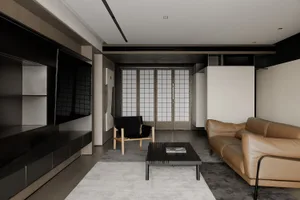 A modern living room with minimalist design, featuring a beige leather sofa, black armchair, and a black coffee table.