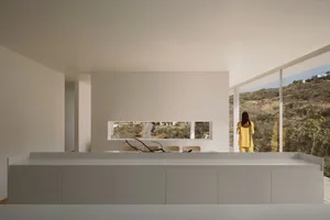 Modern minimalist living room with glass walls and a person in a yellow coat standing by a window.