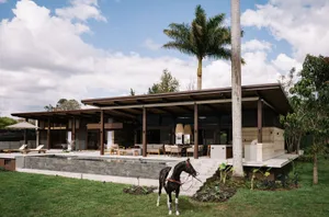 A modern house with a pool, concrete and glass architectural features, surrounded by greenery.