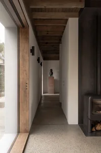 Modern minimalist corridor with concrete floor, wood beams, and floor-to-ceiling windows.