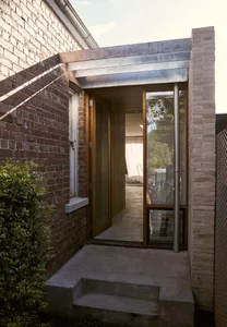 An entrance designed with brick walls, concrete steps, and aluminum framework.
