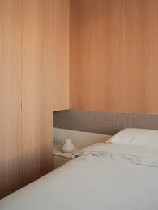 A bedroom with a minimalistic design featuring a monochrome color scheme and a wooden cabinet.