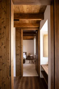 A minimalistic bedroom with wooden walls and ceiling beams, featuring a single bed and a small table.