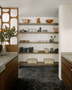 Organized wooden shelves in a minimalist kitchen pantry with botanicals in a vase on the left.
