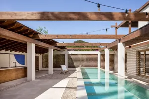 Minimalist residential outdoor space featuring wood pergolas, greenery, and a concrete pool area.