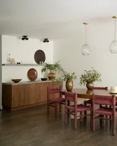 A modern dining room featuring wooden furniture, including a round wooden table, red woven chairs, and a shelf with decorativ