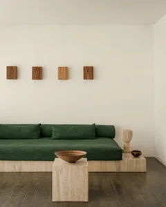 A modern living room with a green upholstered sofa, wooden sculptures, and a wooden coffee table on a wooden floor.