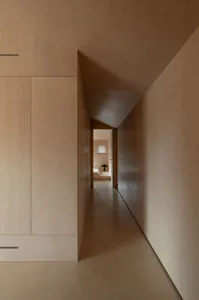 Modern minimalist wooden hallway with light-colored wood paneling and a narrow corridor leading to a bedroom with a small win