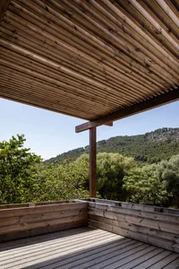 Modern outdoor deck featuring a wooden lattice overhead, surrounded by lush greenery and hills in the background.