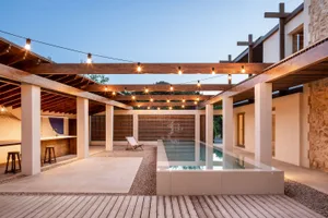 Modern residential patio featuring a wooden deck and stone walls with a glass wall and light fixtures hanging above.
