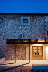 A stone building entrance with a wooden pergola at dusk.