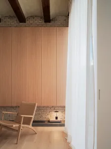 A minimalist living room with wooden paneling, a woven chair, and a bookshelf.