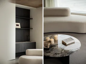 A modern living room with a white couch, a circular marble coffee table with candles and a book, and a dark wooden shelving u