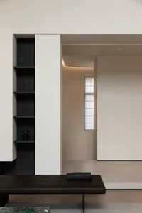A minimalist interior showcasing a white concrete wall and floor, with a black shelf and a black bench.