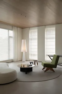 A minimalist modern living room with concrete walls, a glass coffee table, and wooden accents.
