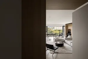 Modern living room with light wooden flooring, white sofa, black chair, and large windows.