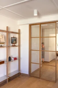 Modern minimalist living room featuring a glass and wooden sliding door, sleek flooring, and functional furniture.