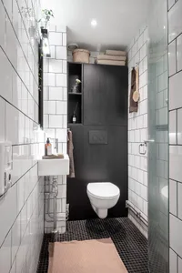 A minimalist bathroom with black and white tiles, featuring a sink, toilet, and shower.