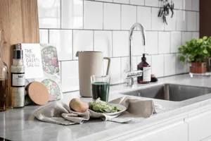 A modern kitchen with a marble countertop, featuring a glass pitcher, green smoothie, pears, and a plate with leafy greens an