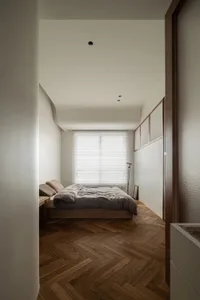A minimalist bedroom featuring a low wooden bed platform and a wooden floor with a herringbone pattern.