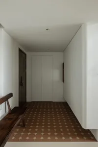 A minimalist entryway featuring a tiled floor and wooden bench against white walls.