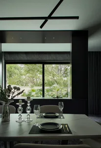 A minimalist dining room with white marble table, glass candlesticks, and a view of greenery through large windows.