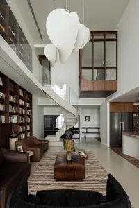 A modern living room featuring concrete flooring, a spiral staircase made of glass and wood, and dark leather sofas.