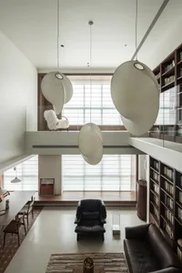 A modern living room featuring a unique hanging light fixture and a library shelving unit filled with books.