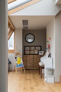 A modern music room with oak furniture featuring a piano, easel with artwork, and a clock on the wall.