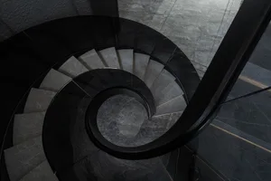 A modern spiral staircase featuring glass railings and steps, set against a dark background.