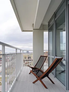 A minimalist balcony with wooden chairs and a view of a cityscape.