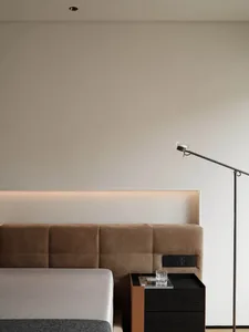 A minimalist bedroom featuring a velvet headboard and wooden bedside table with a modern floor lamp.