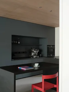 A modern kitchen featuring sleek black steel cabinets, a countertop espresso machine, and a red chair.