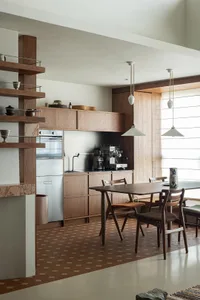 A modern kitchen with wooden cabinets, a wooden table, and pendant lights.