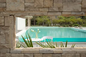 Modern residential outdoor area featuring white chairs, a white table, a vase of white flowers, and a view of a clear turquoi