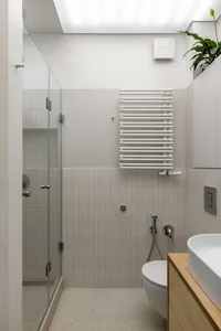 A minimalist bathroom with white tiles and a glass shower enclosure.