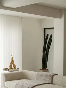 Neutral-toned minimalist living room with a grey sofa, gold sculpture, and tall green cactus plant.